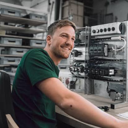 Junger Mann beim Arbeiten an zwei kleinen elektronischen Kabeln am Schreibtisch