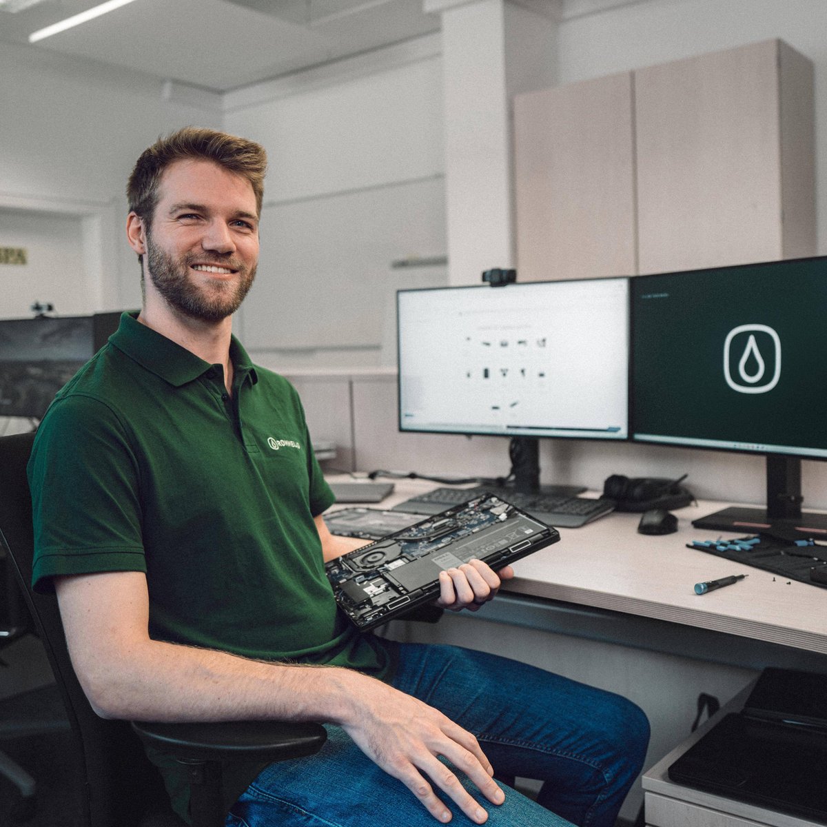 Man with electronic component sitting at a desk, smiling and looking at the camera