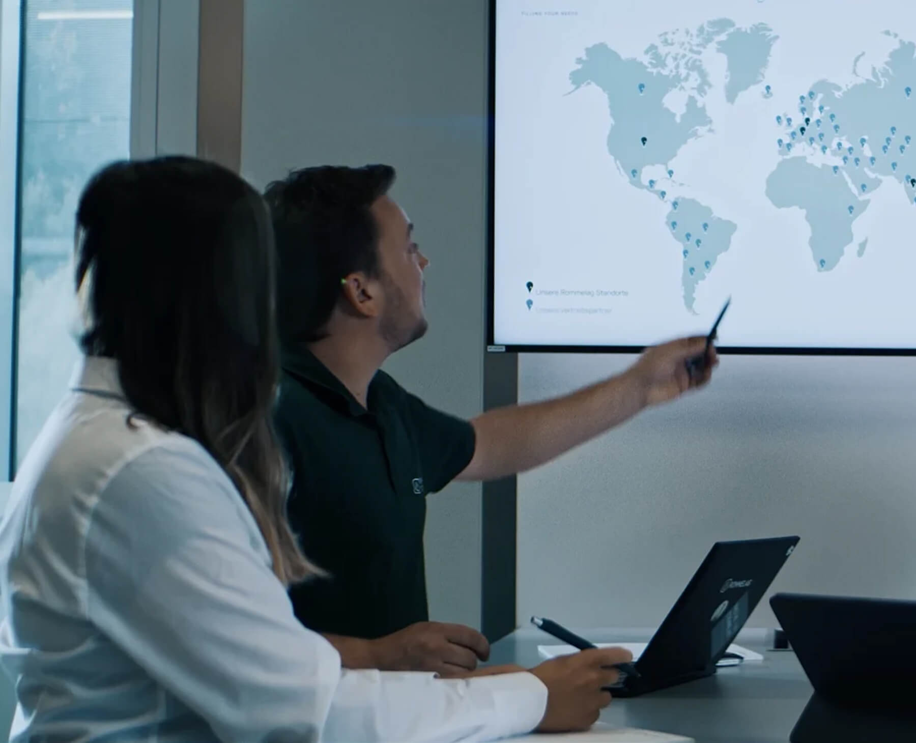 Dois colegas estão discutindo, um ao lado do outro, em um ambiente de escritório profissional. Um deles está gesticulando enquanto o outro ouve atentamente. Ambos parecem concentrados e cooperativos.