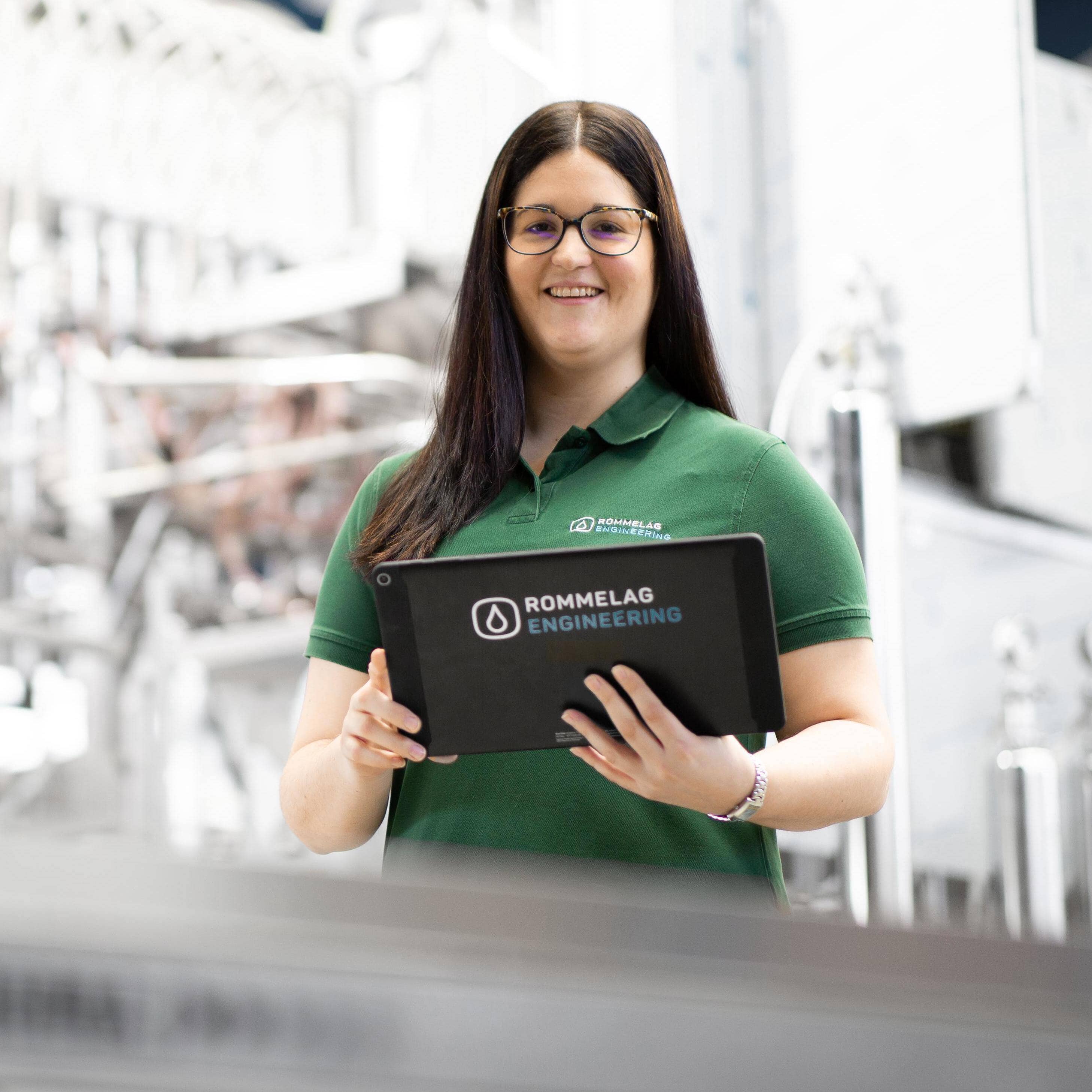 Frau mit Rommelag Tablet in der Hand - in einer Maschinenhalle stehend